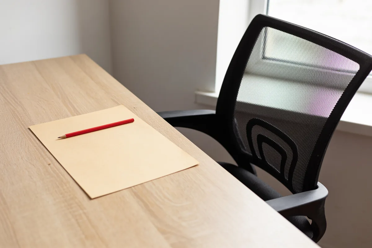 A desk with a chair pulled out, a blank sheet and a red pencil