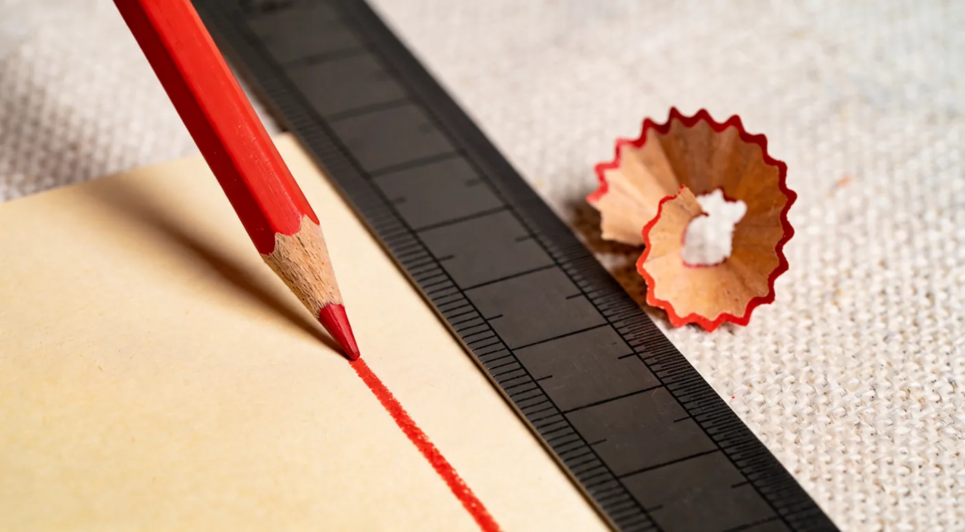 A red pencil drawing one straight line against a steel rule